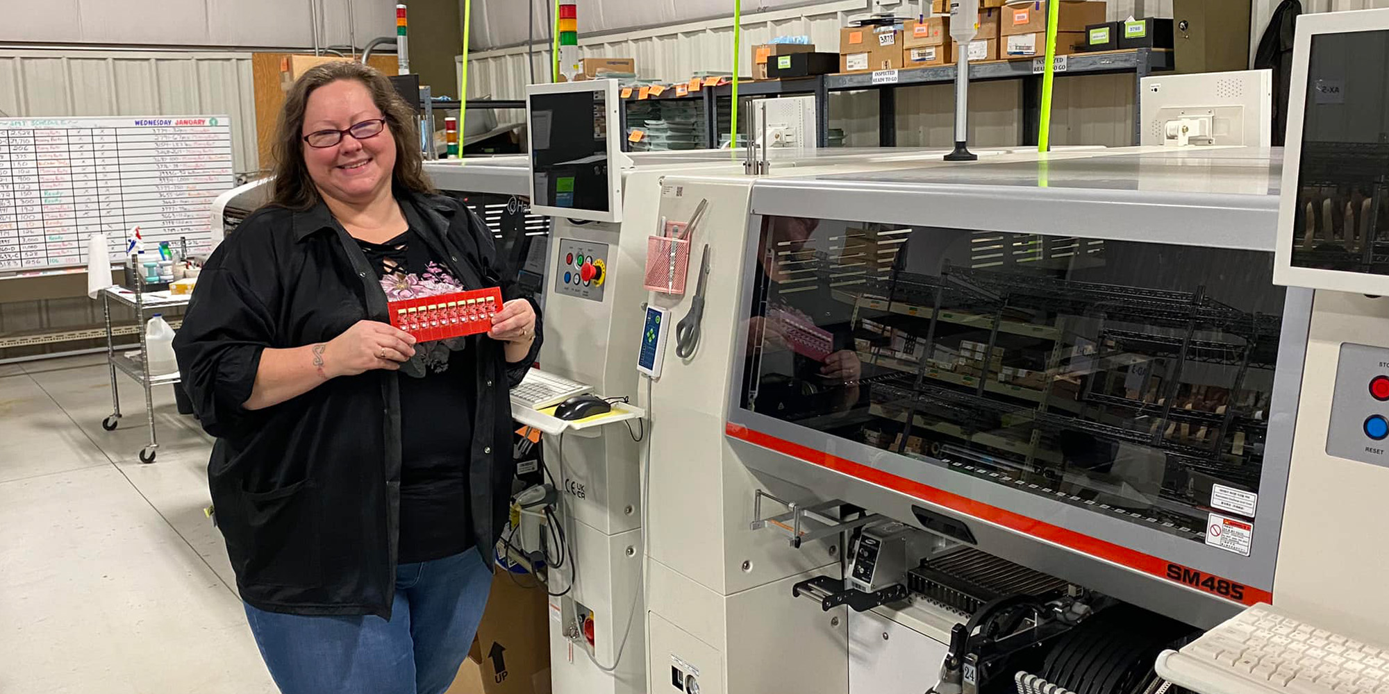 Employee proudly holding PCB Board in front of SMT equipment